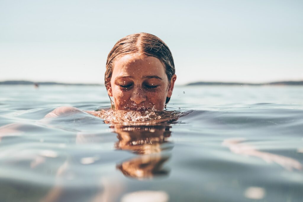 Eine junge, hübsche und sportliche Frau schwimmt mit nassen Haaren im Wasser und entspannt sich.